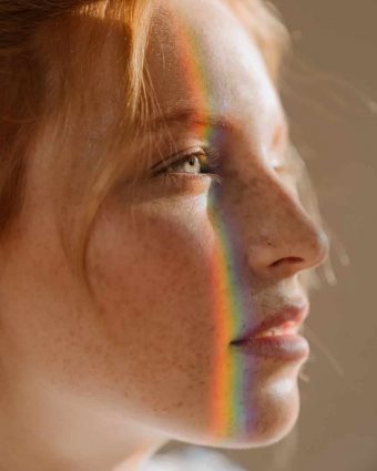 A woman staring off in the distance while a rainbow glows across her face in a vertical fashion.