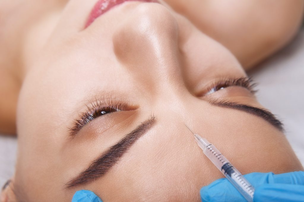 Closeup Portrait of young Caucasian woman getting cosmetic injection of botox in forehead. People