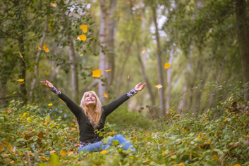 Image of a woman sitting in a field throwing up fall leaves.